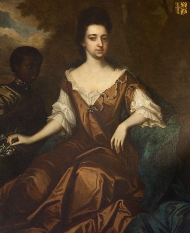 A formal portrait painting featuring a woman with pale skin seated in an ornate dress with brown fabric and white lace accents. Accompanying her, slightly behind her and on the left, is a boy with dark skin, dressed in dark clothing and a metallic collar around his neck.