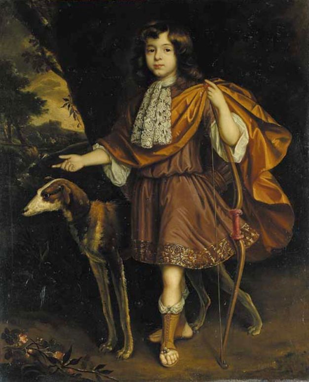 A boy with dark skin is visible from the chest up. He is angled to our right and looks in that direction. He is dressed in dark clothing with shiny accents and ears a metallic collar around his neck.