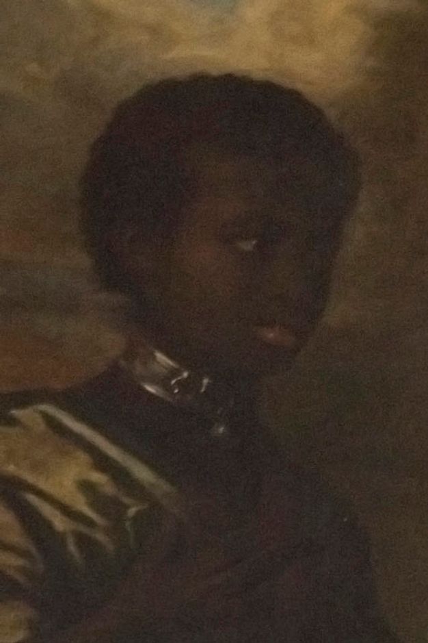 Portrait of a person wearing a dark, high-collared outfit with a metallic choker around their neck. The background is blurred with earthy tones, creating a soft ambiance. The lighting emphasizes shadows, lending an air of mystery to the subject's expression.