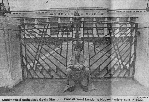 Newspaper clipping with a black and white photograph of a man in a trench coat sitting in front of a wrought-iron gate. A large white building with columns all along the facade and the words "Hoover Limited" above is in the background.